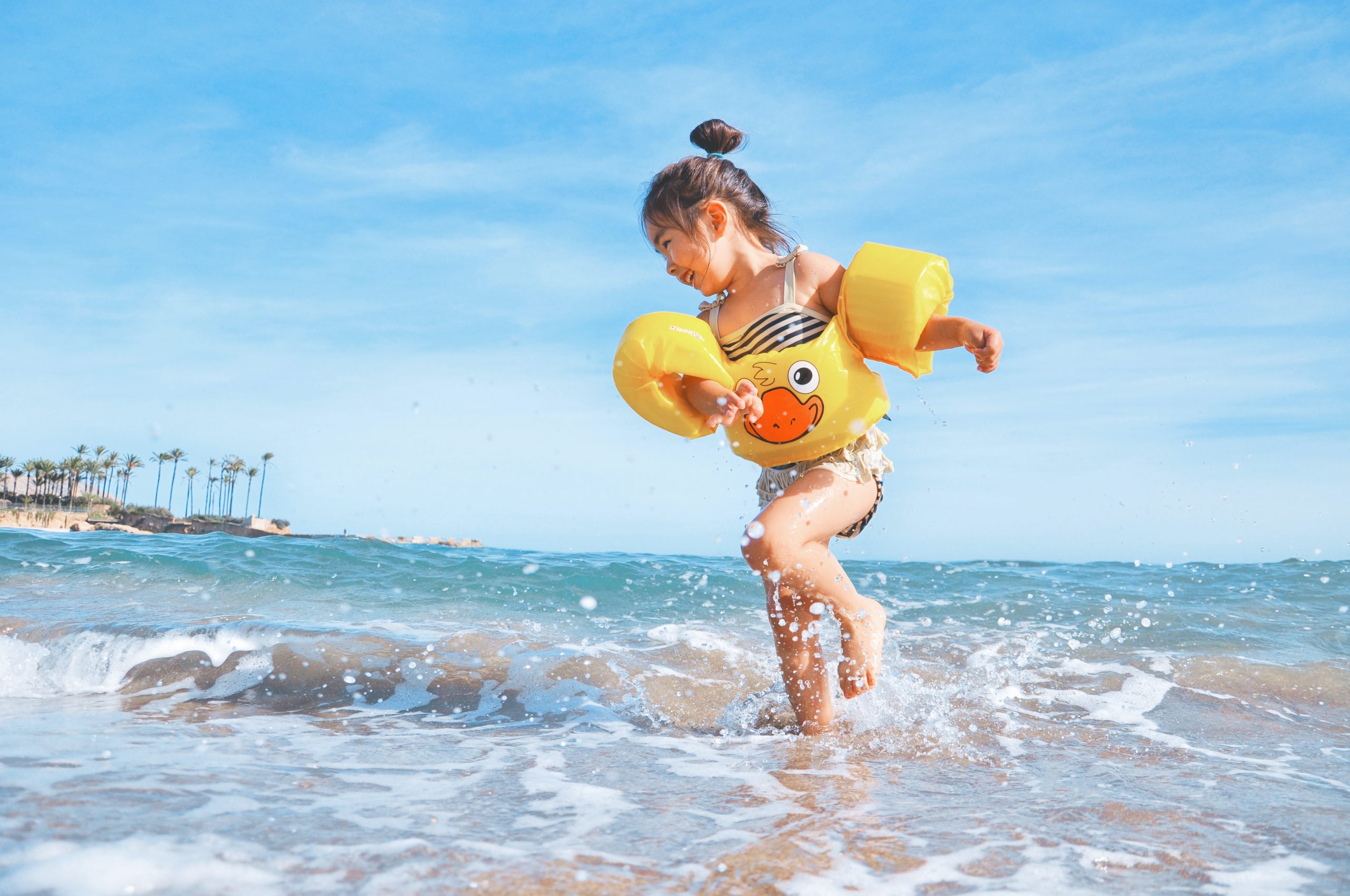 baby playing on beach in the waves with floaties on